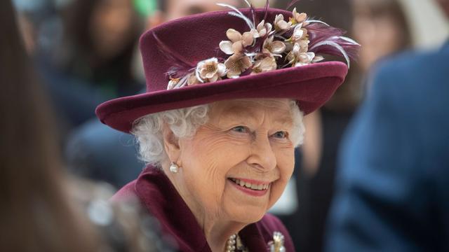 Die britische Königin Elizabeth II. lächelt mit violettem Hut zum gleichfarbigen Kostüm. 