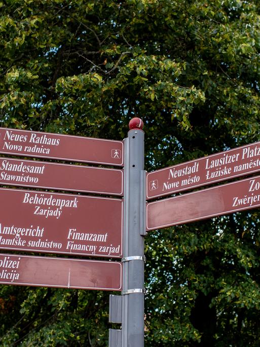 Ein Wegweiser mit braunen Schildern, deren Ziele jeweils auf deutsch und sorbisch beschriftet sind.
