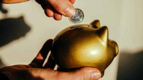 Eine Frauenhand steckt einen Euro in ein goldenes Sparschwein.
