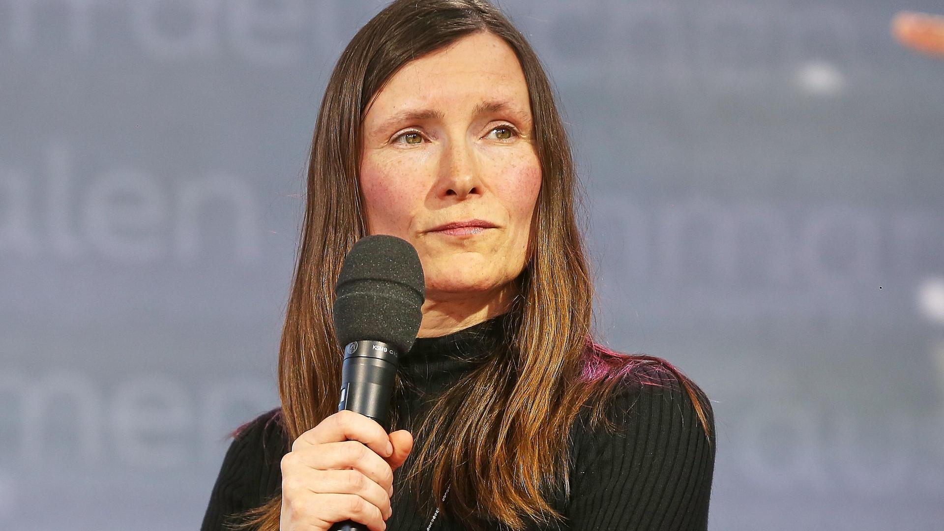 Heike Geißler mit langen braunen Haaren guckt mit einem Mikrofon in der Hand auf der Leipziger Buchmesse zur Seite