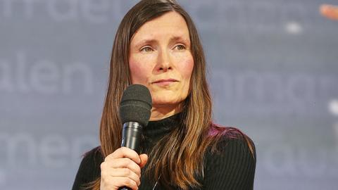 Heike Geißler mit langen braunen Haaren guckt mit einem Mikrofon in der Hand auf der Leipziger Buchmesse zur Seite