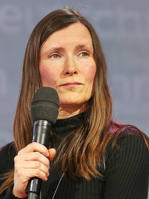 Heike Geißler mit langen braunen Haaren guckt mit einem Mikrofon in der Hand auf der Leipziger Buchmesse zur Seite
