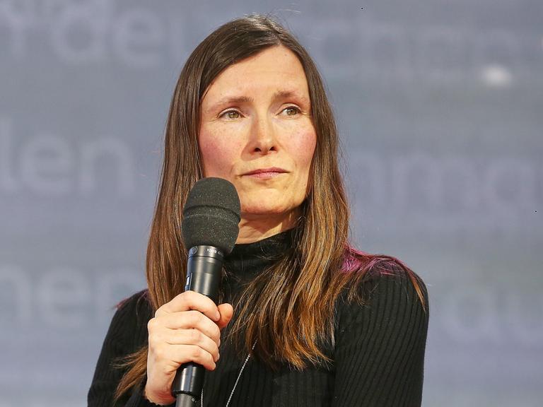 Heike Geißler mit langen braunen Haaren guckt mit einem Mikrofon in der Hand auf der Leipziger Buchmesse zur Seite