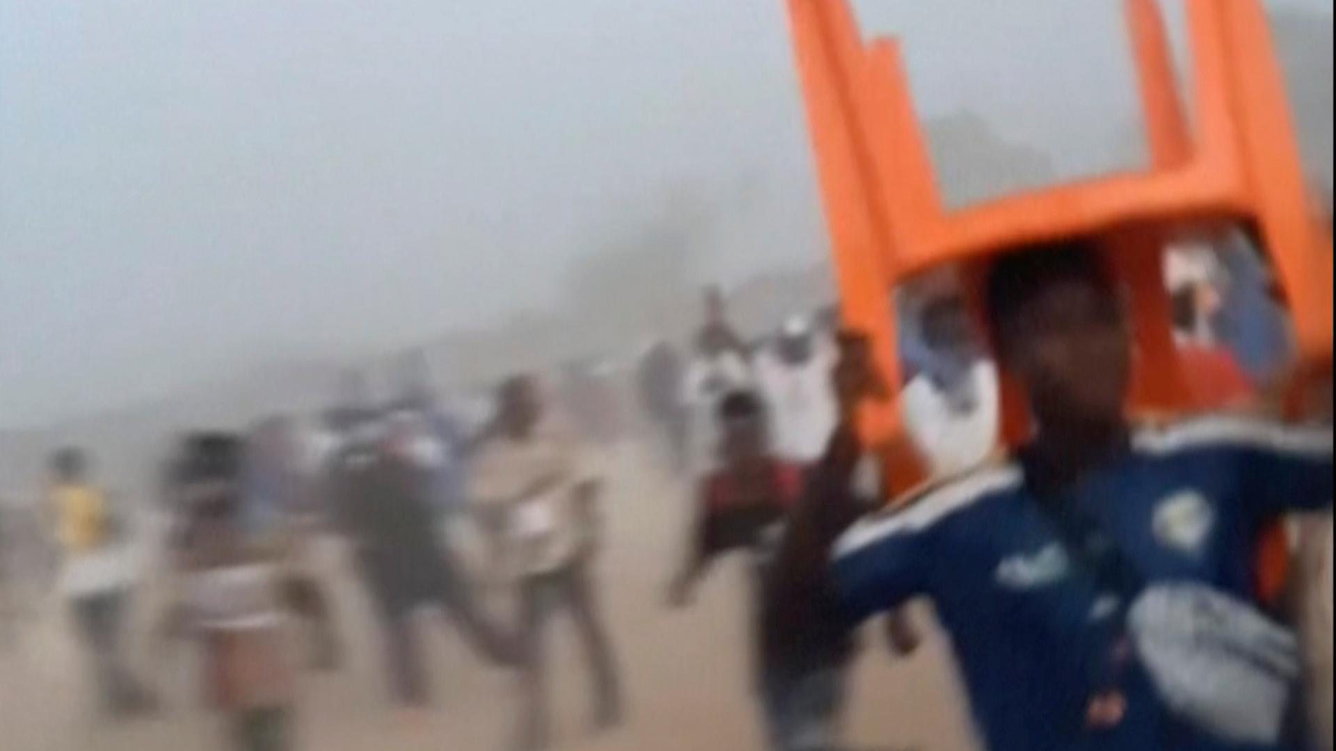 Guinea: Dieses Standbild aus einem von Nimba Sports Zaly zur Verfügung gestellten Video zeigt einen Mann, der mit einem Stuhl über dem Kopf während einer Massenpanik unter Fußballfans das Stadion verlässt.