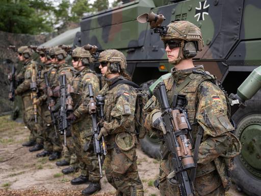 Bewaffneten Grenadiere stehen auf einem Bundeswehrgelände vor einem Militärfahrzeug.