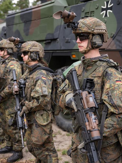 Bewaffneten Grenadiere stehen auf einem Bundeswehrgelände vor einem Militärfahrzeug.
