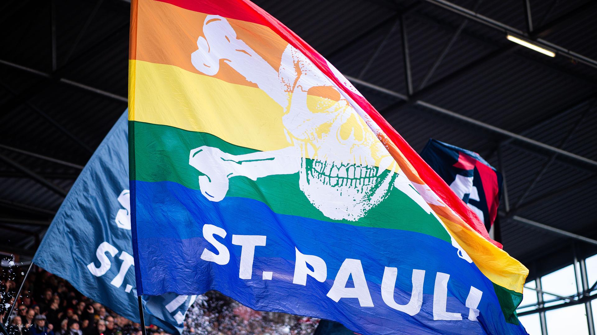 Fans von Sankt Pauli halten eine Regen-Bogen-Flagge von den Fußball-Club. Auf der Flagge ist auch ein Totenkopf. 