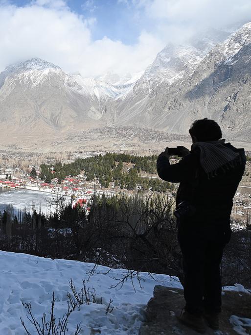 Ein Mann macht Fotos von einer verschneiten Berglandschaft.