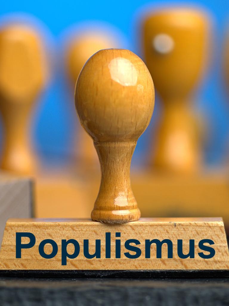 Ein Holzstempel mit der Aufschrift "Populismus" auf einer Schieferplatte mit weiteren Stempeln unscharf dahinter vor einem blauen Hintergrund. Ein Holzstempel mit der Aufschrift "Populismus" auf einer Schieferplatte mit weiteren Stempeln unscharf dahinter vor einem blauen Hintergrund.