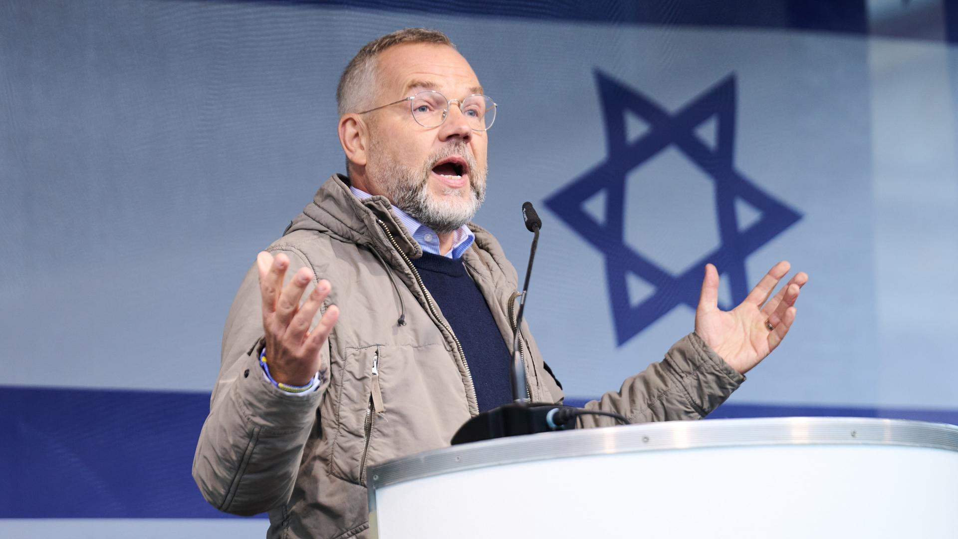 Der SPD-Außenpolitiker Michael Roth spricht auf der Solidaritätskundgebung für Israel in Berlin. Im Hintergrund die israelische Fahne. 