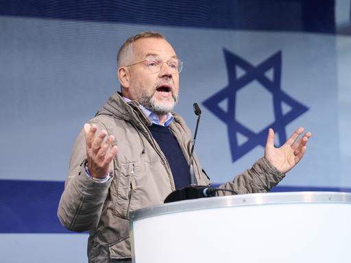 Der SPD-Außenpolitiker Michael Roth spricht auf der Solidaritätskundgebung für Israel in Berlin. Im Hintergrund die israelische Fahne. 