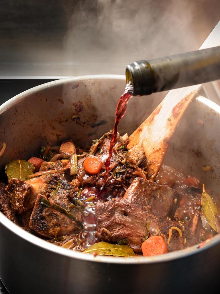 Rotwein wird in einen dampfenden Edelstahltopf gegossen, um die gebratenen Zutaten wie Knochen, Fleisch und Gemüse abzulöschen