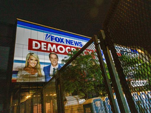 Ein Banner von Fox News hängt an einem Gebäude. Darauf zu sehen: eine Frau und ein Mann sowie der Schriftzug „Fox News“ und „Democracy“. 