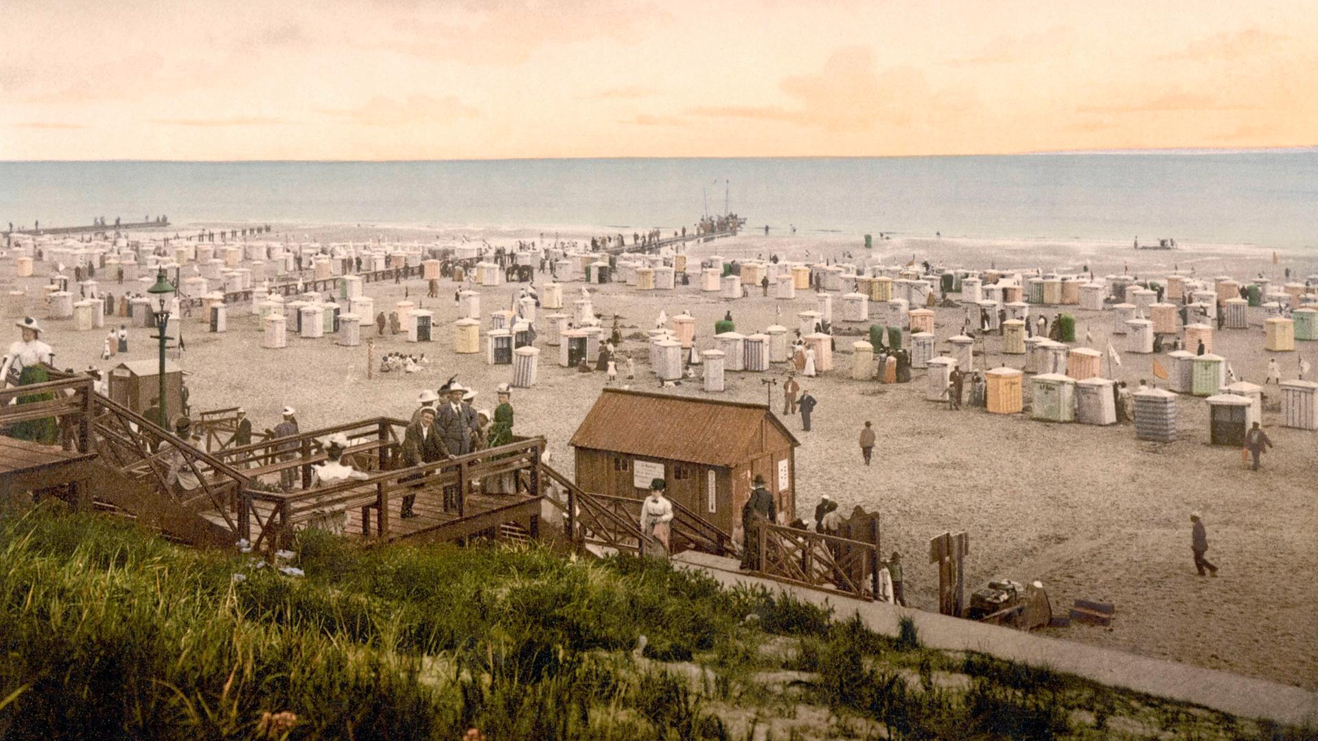 Nachkolorierte historische Aufnahme zeigt den Strand von Borkum mit Kurgästen um 1900. 