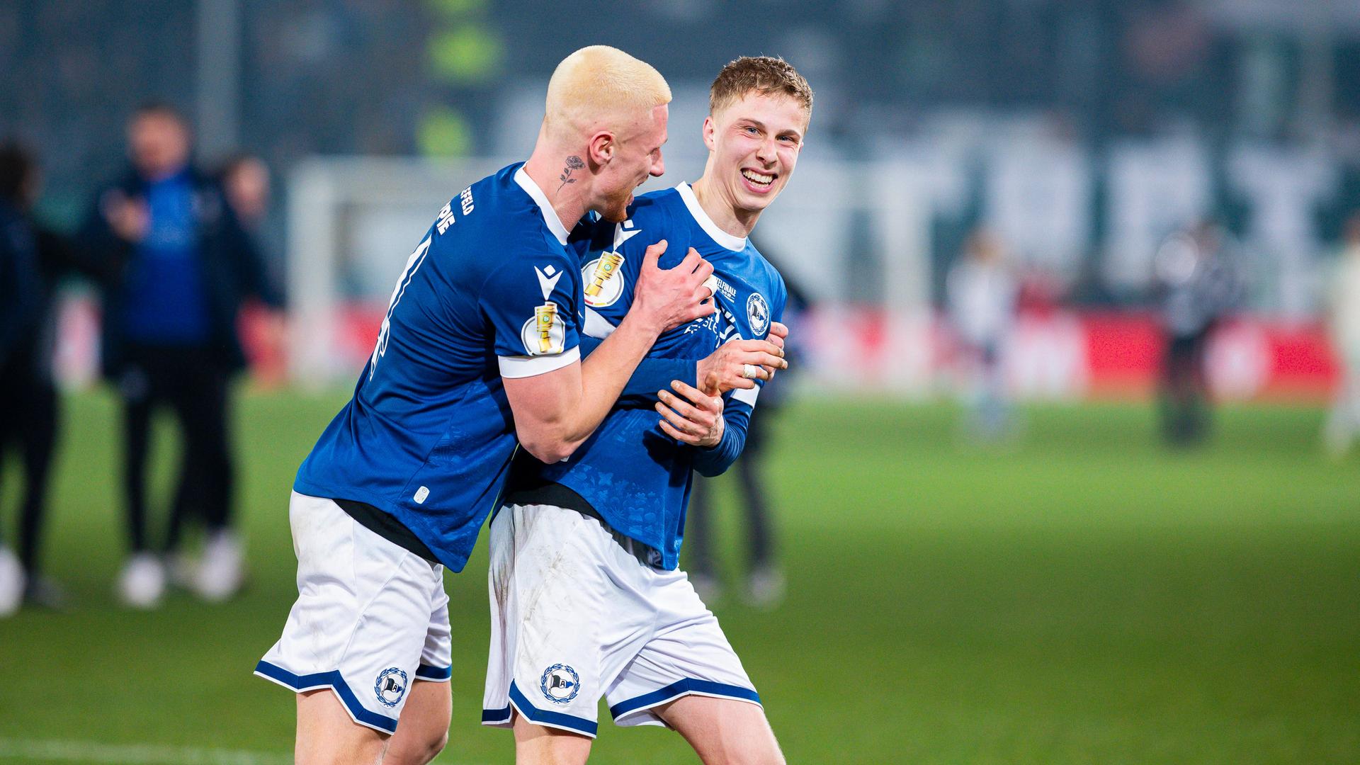 2 Fußball-Spieler in Trikots freuen sich.