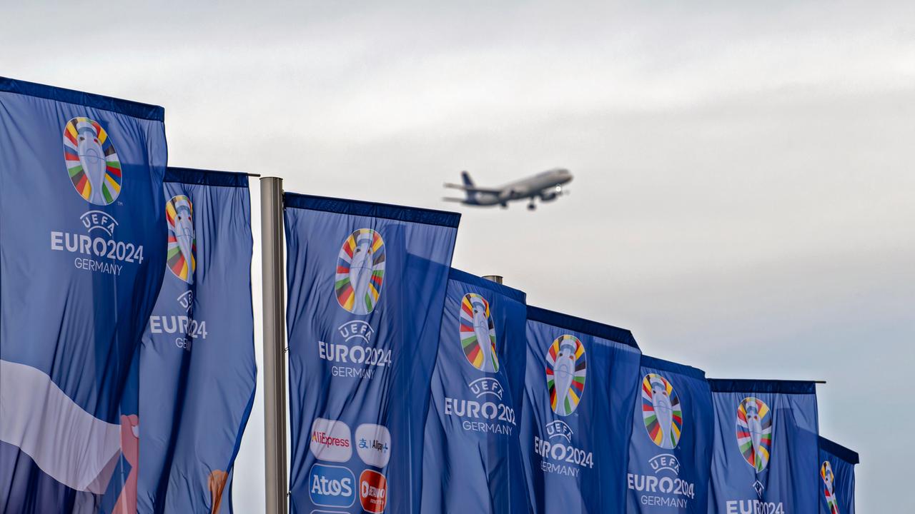 Wehende Fahnen der UEFA Euro 2024, im Hintergrund ist ein Flugzeug im Landeanflug zu sehen.