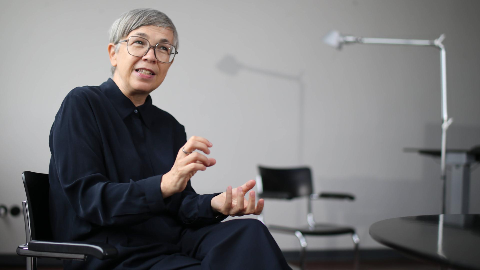 Barbara Steiner sitzt lächelnd und gestikulierend in einem Bürostuhl.