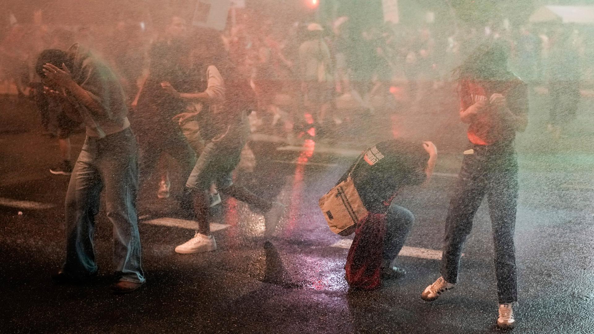 Junge Menschen ducken sich von einem Wasserstrahl aus einem Wasserwerfer der Polizei weg. Sie protestieren gegen die israelische Regierung.