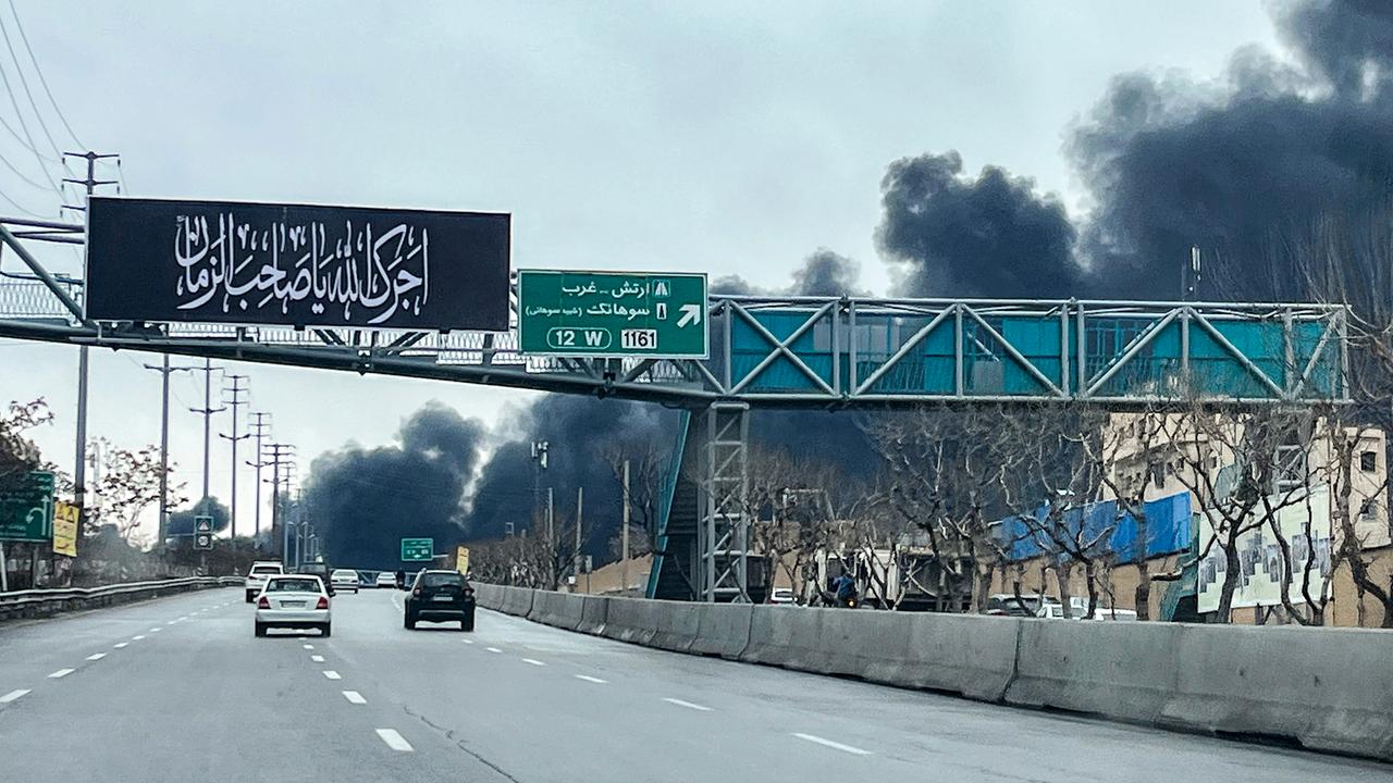 Auf einer mehrspurigen Straße fahren Autos. Im Hintergrund steigt dichter, schwarzer Rauch auf.