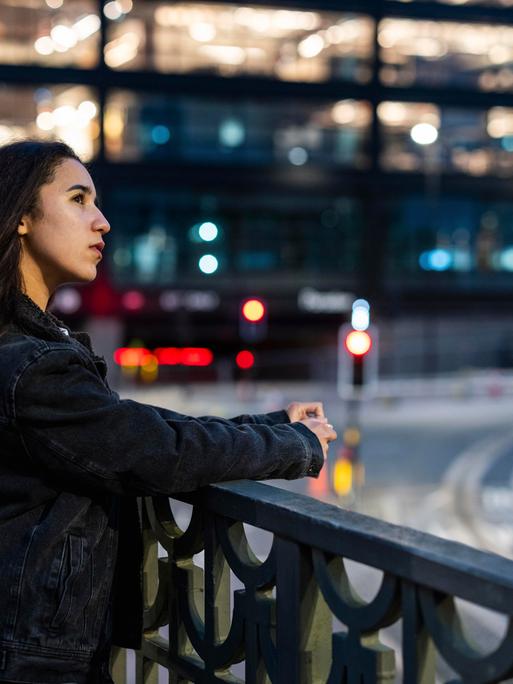 Eine Frau blickt in einer Stadt an einer breiten Kreuzung von einer Brücke in die Ferne.