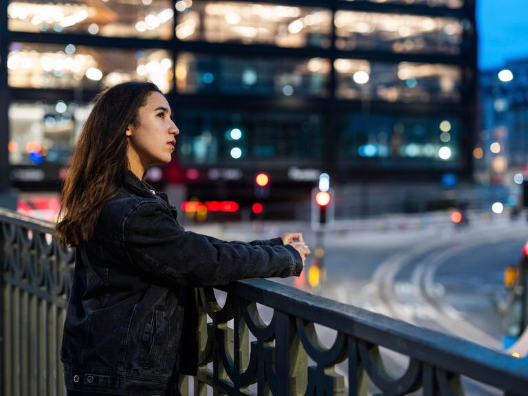 Eine Frau blickt in einer Stadt an einer breiten Kreuzung von einer Brücke in die Ferne.