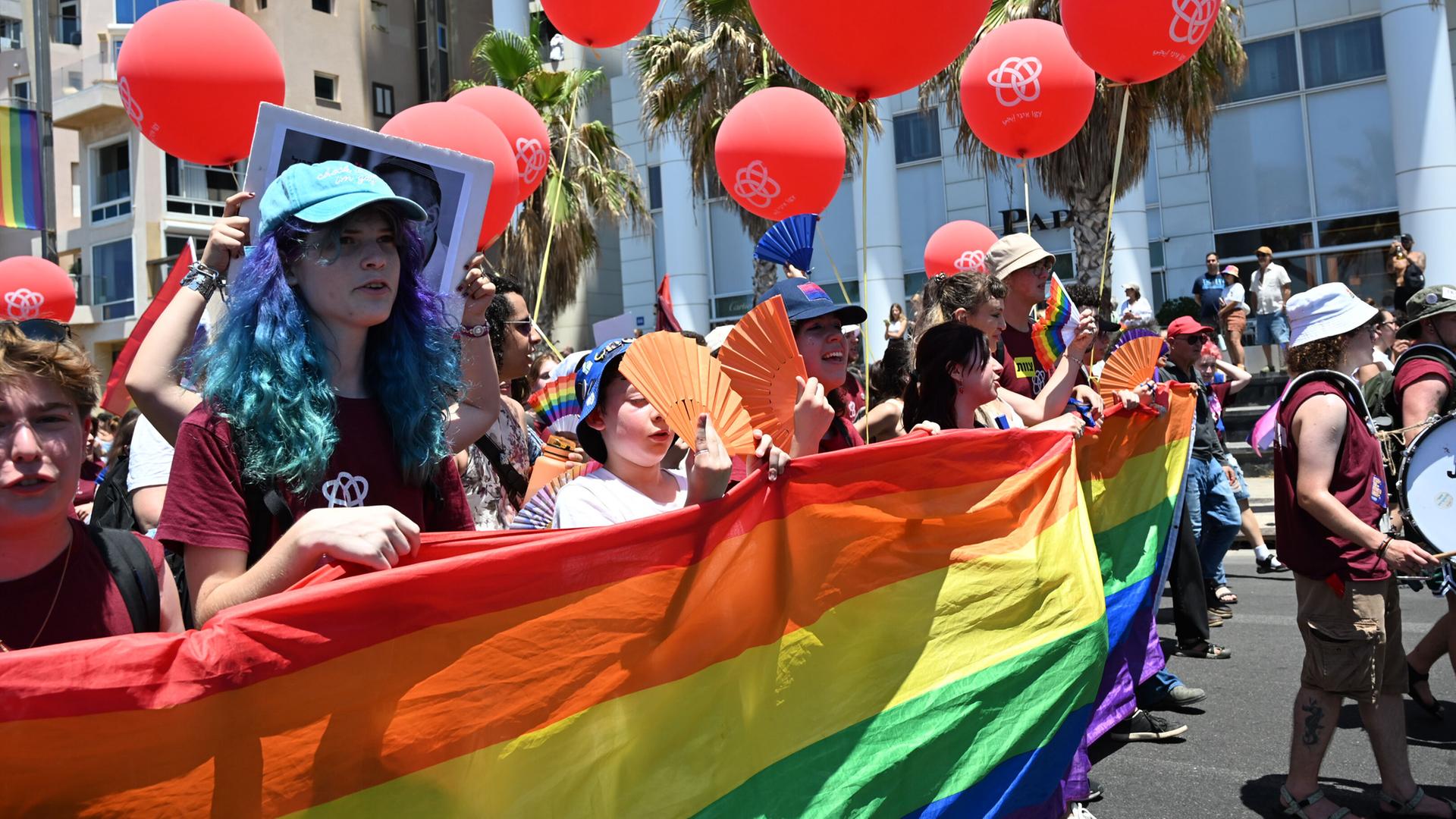Das Bild zeigt Teilnehmer der Pride Parade in Tel Aviv, die ein Regenbogenbanner tragen. Das Bild zeigt Teilnehmer der Pride Parade in Tel Aviv, die ein Regenbogenbanner tragen.