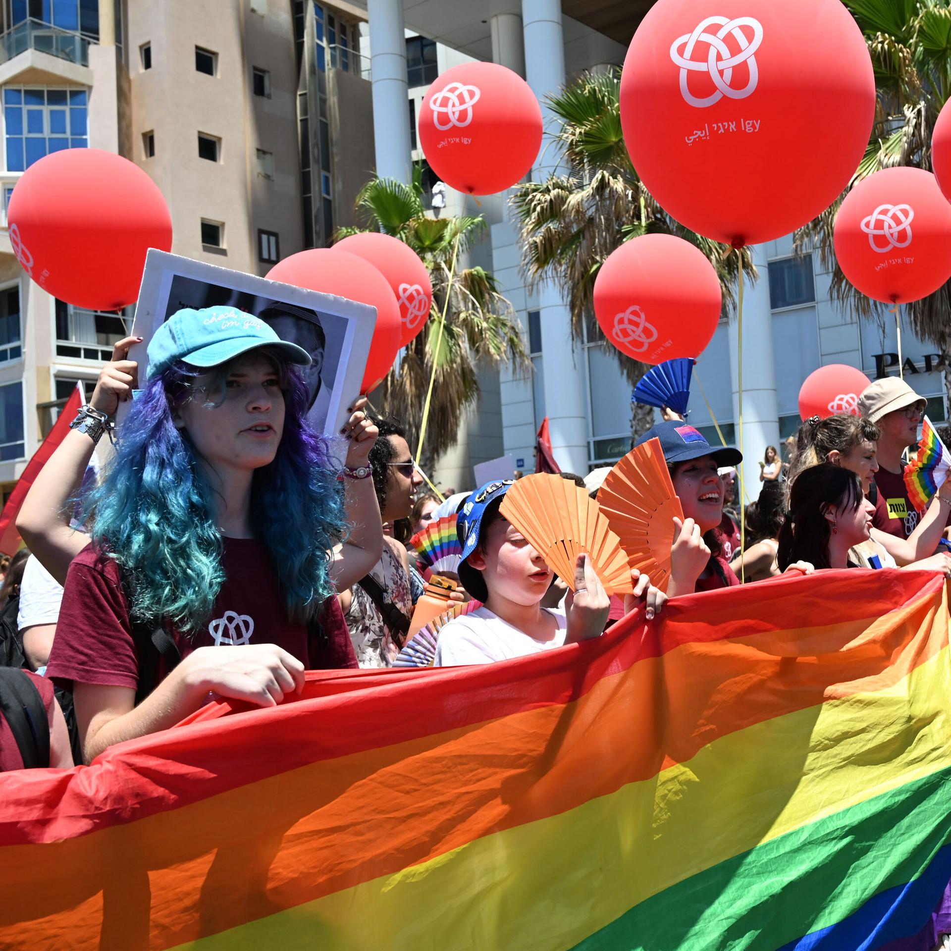 Das Bild zeigt Teilnehmer der Pride Parade in Tel Aviv, die ein Regenbogenbanner tragen. 