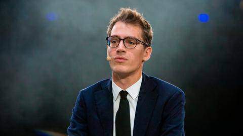 Arthur Mensch in Anzug und Krawatte, vor grün-gräulichem Hintergrund. Er trägt eine Brille und schaut in Richtung der Kamera, allerdings leicht vorbei.