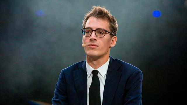 Arthur Mensch in Anzug und Krawatte, vor grün-gräulichem Hintergrund. Er trägt eine Brille und schaut in Richtung der Kamera, allerdings leicht vorbei.