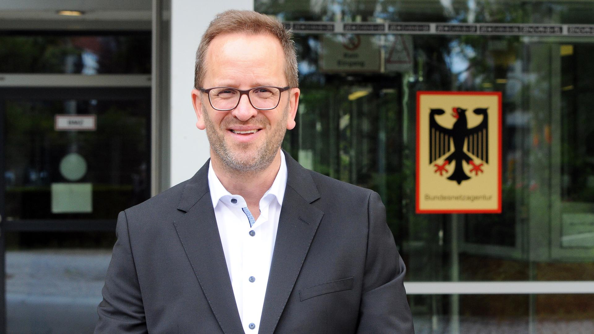 Das Foto zeigt Klaus Müller, Präsident der Bundesnetzagentur. Er steht vor dem Eingang des Dienstsitzes der Bundesbehörde.
