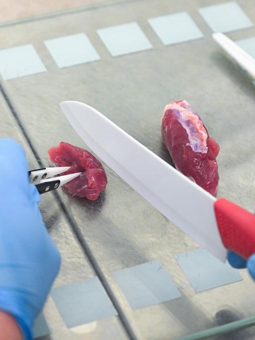 Ein Stück Fleisch wird mit einem Messer in zwei Stücke geteilt. 