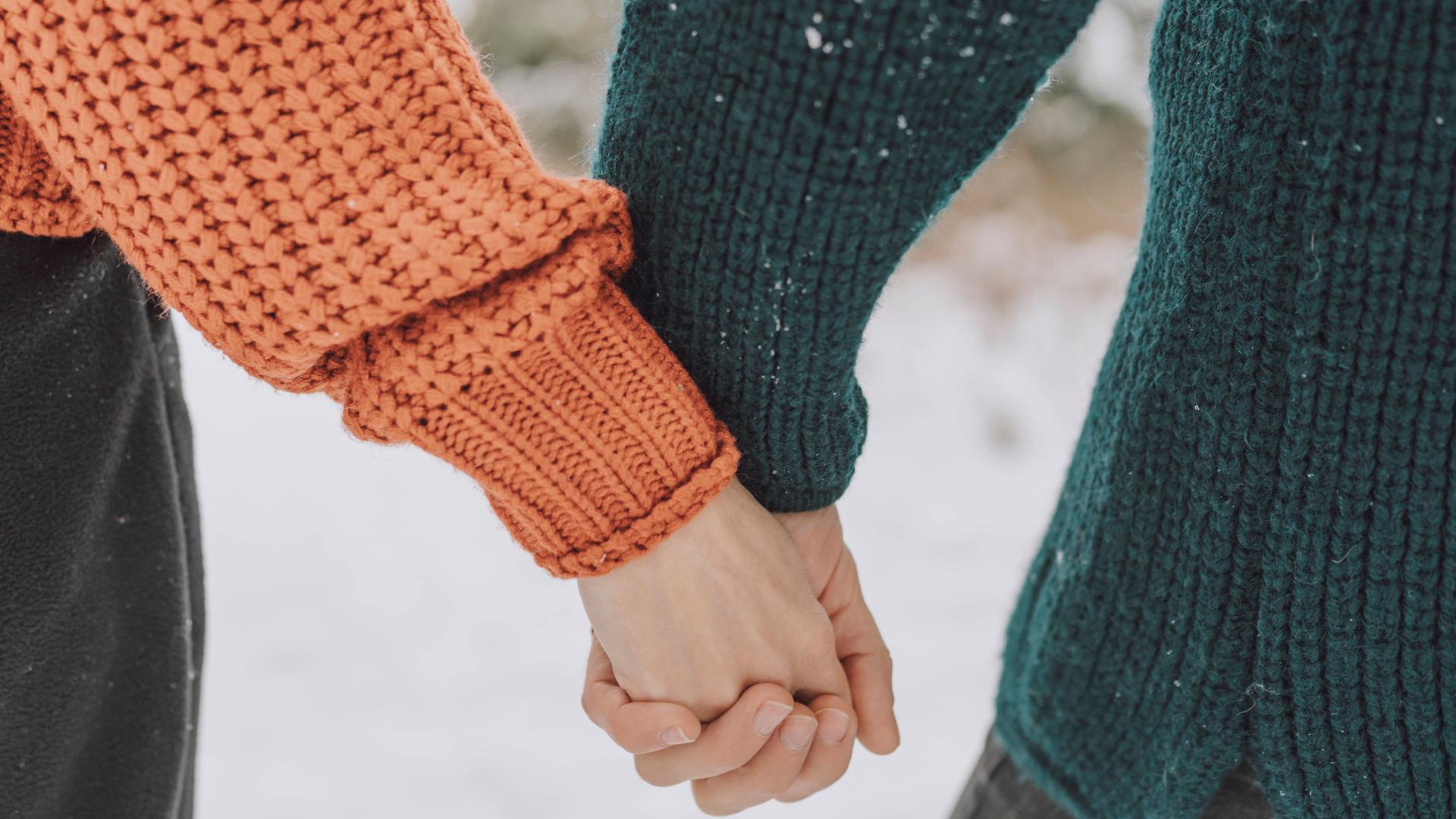 Man sieht die Arme eines Paares, das Händchen hält, im Schnee.