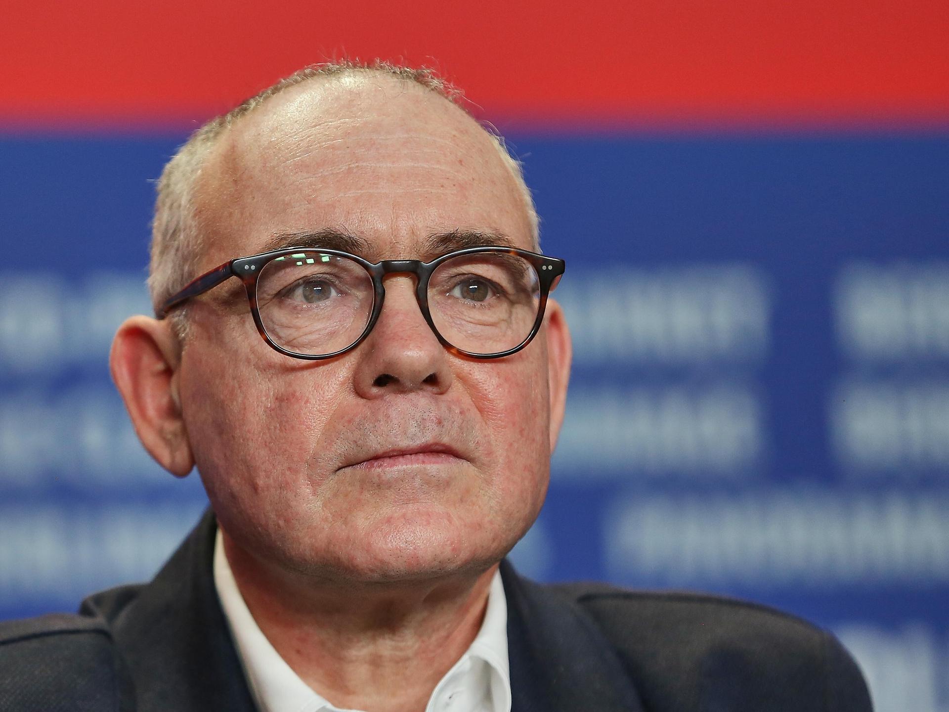 Christophe Boltanski trägt eine schwarze Brille und sitzt vor einem blau-roten Fotohintergrund bei einer Pressekonferenz