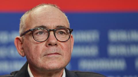 Christophe Boltanski trägt eine schwarze Brille und sitzt vor einem blau-roten Fotohintergrund bei einer Pressekonferenz