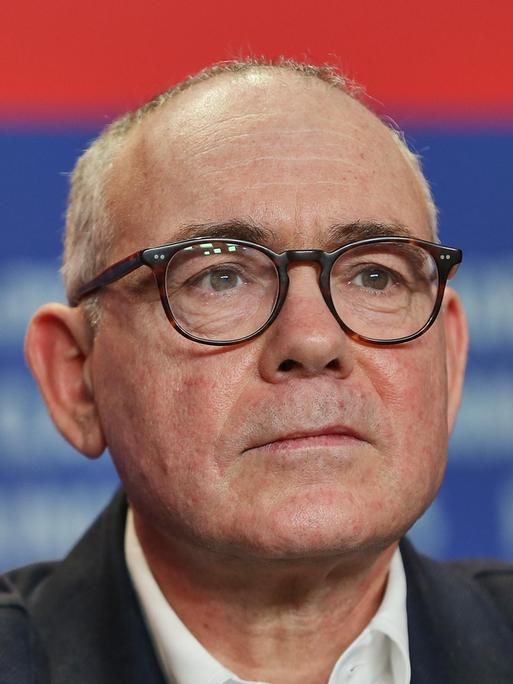 Christophe Boltanski trägt eine schwarze Brille und sitzt vor einem blau-roten Fotohintergrund bei einer Pressekonferenz