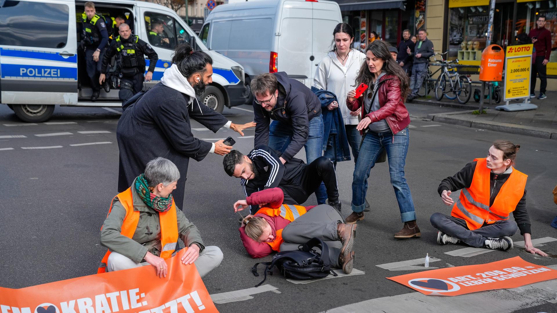 Eine Aktivistin der Gruppe Letzte Generation wird bei einer Blockade-Aktion am Berliner Hermannplatz angegriffen, die Polizei kommt hinzu.