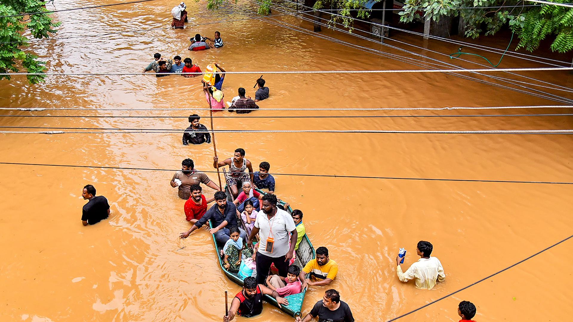 Einige Menschen sitzen in einem Boot, andere laufn durch das brusthohe schlammige Wasser in Vijayawada in Indien.