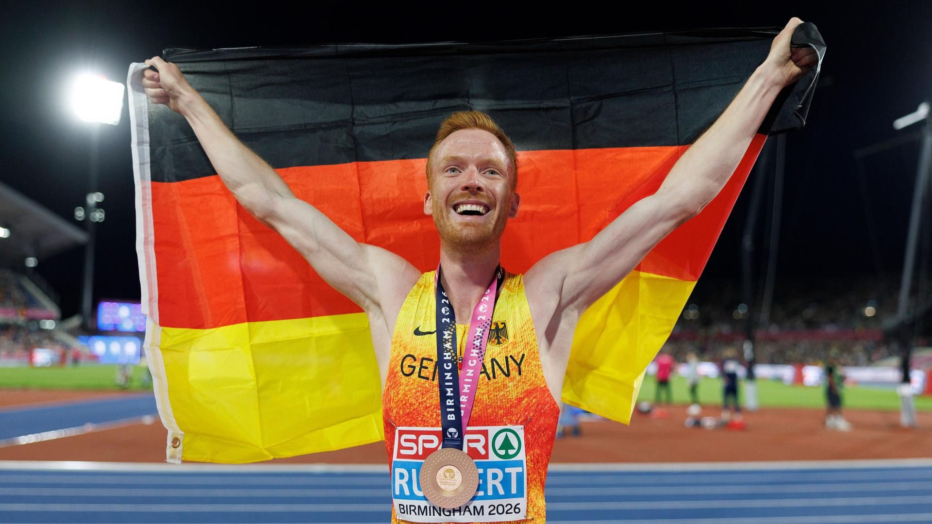 Der deutsche Läufer Frederik Ruppert jubelt mit der Deutschlandflagge in den Händen.