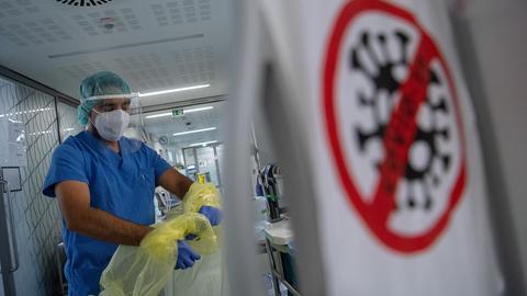 Ein Pfleger zieht sich beim Verlassen der Intensivstation für Corona-Patienten in einem Krankenhaus seinen Schutzkittel aus.