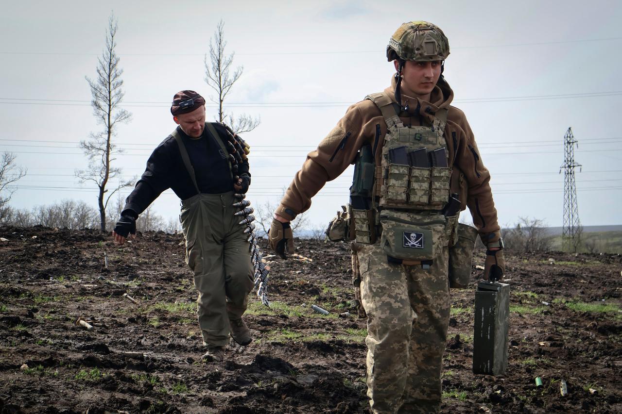 Zwei Soldaten laufen über eine matschige Fläche. Der vordere trägt einen grünen Metallkoffer, der hintere einen Patronengurt über der Schulter.