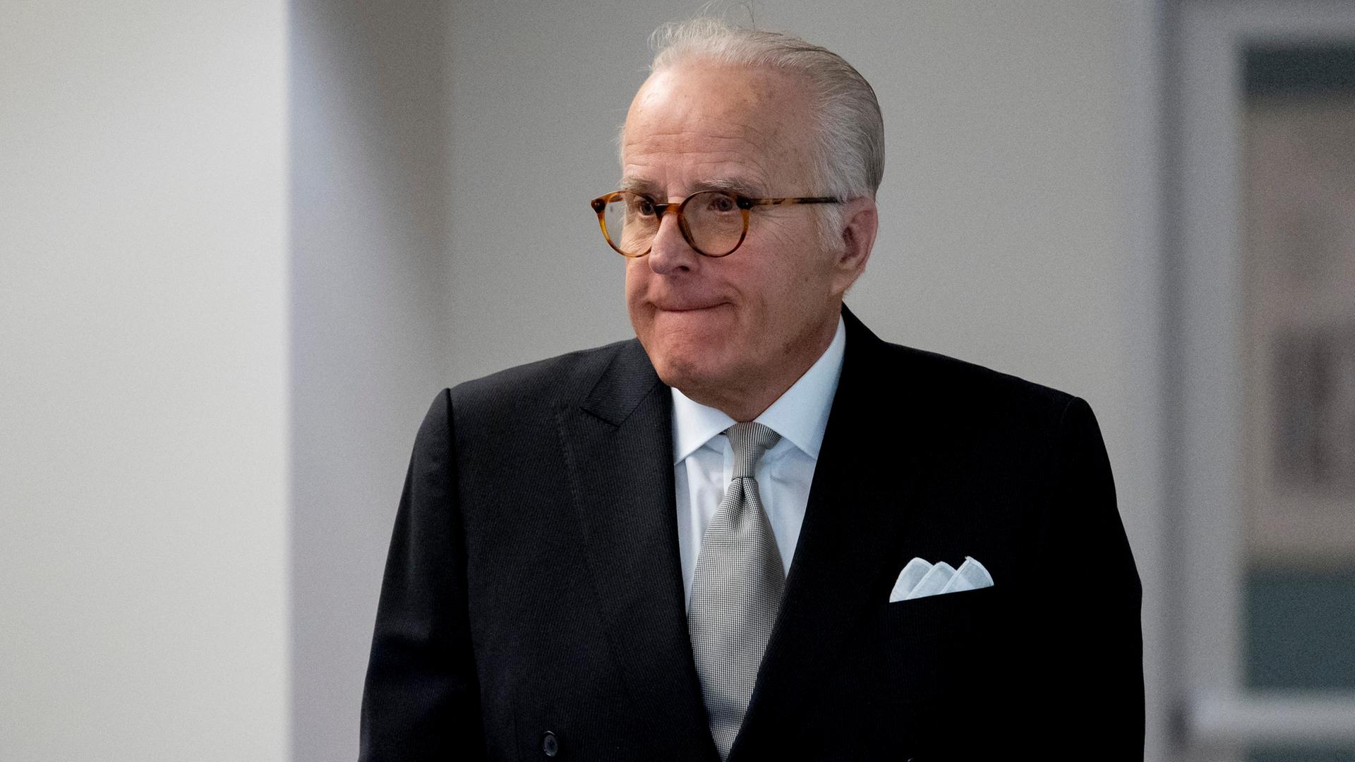 Der grauhaarige James Biden im schwarzen Jacket mit Krawatte und brauner Brille steht vor einer weißen Außenwand. Er kneift die Lippen zusammen. Der grauhaarige James Biden im schwarzen Jacket mit Krawatte und brauner Brille steht vor einer weißen Außenwand. Er kneift die Lippen zusammen.