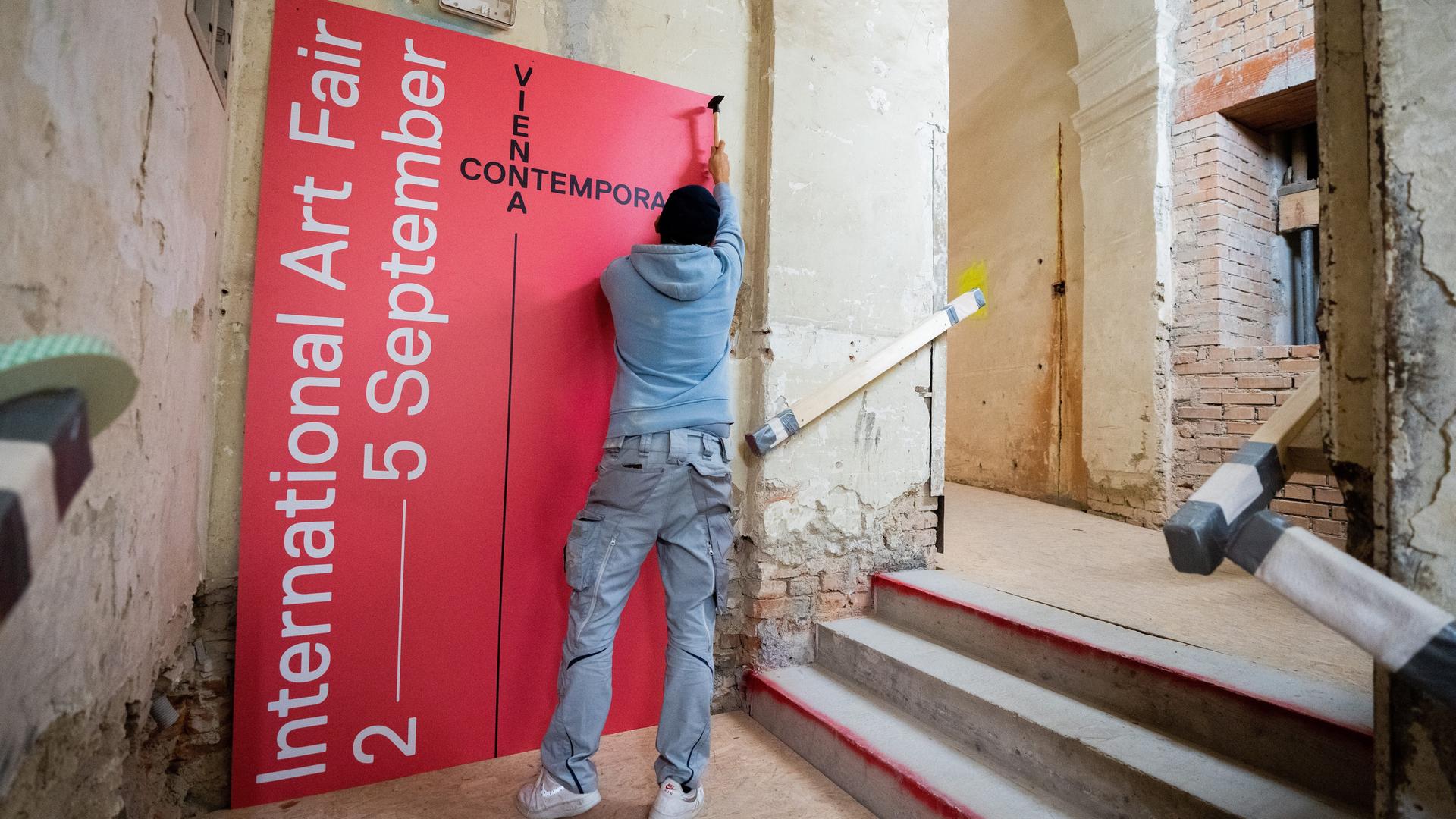 Ein Mann hängt in einem nur teils renovierten Raum ein Plakat der viennacontemporary auf
