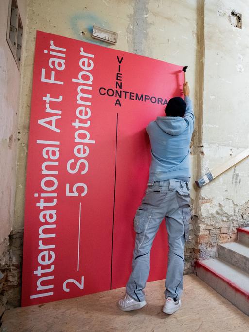 Ein Mann hängt in einem nur teils renovierten Raum ein Plakat der viennacontemporary auf
