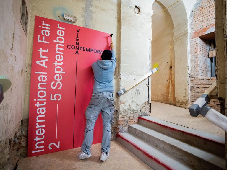 Ein Mann hängt in einem nur teils renovierten Raum ein Plakat der viennacontemporary auf