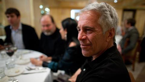 Der verstorbene Investmentbanker und verurteilte Sexualstraftäter Jeffrey Epstein im Porträt an einem gedeckten Tisch mit Personen im Hintergrund. 
