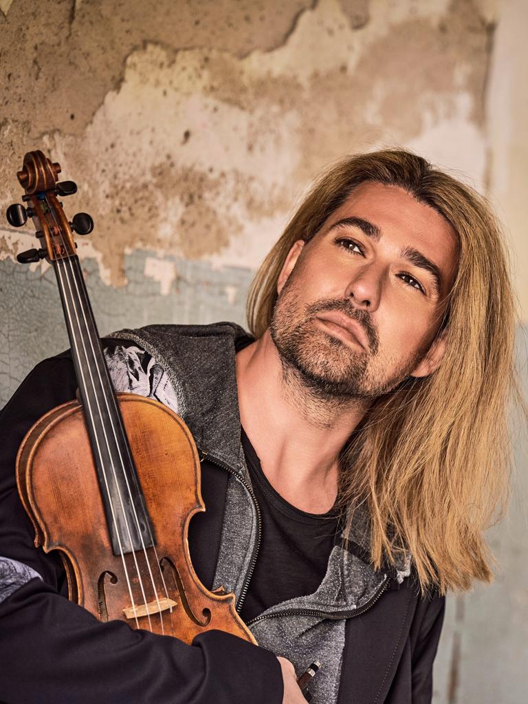 Ein Mann mit blonden, halblangen Haaren, im Arm eine Geige. Er steht in einem alten Gebäude, der Putz blättert ab, er schaut versonnen in die Ferne.