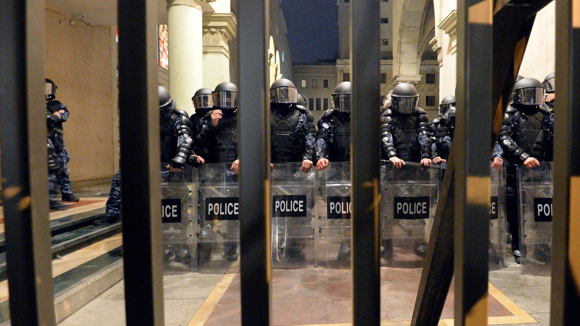 Eine Reihe Polizisten in voller Montur steht hinter einem Tor in Tiflis.