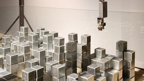 Ein Robotergreifarm schwebt über Metallwürfeln.