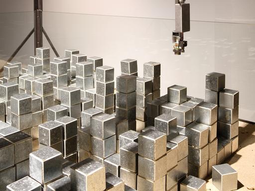 Ein Robotergreifarm schwebt über Metallwürfeln.