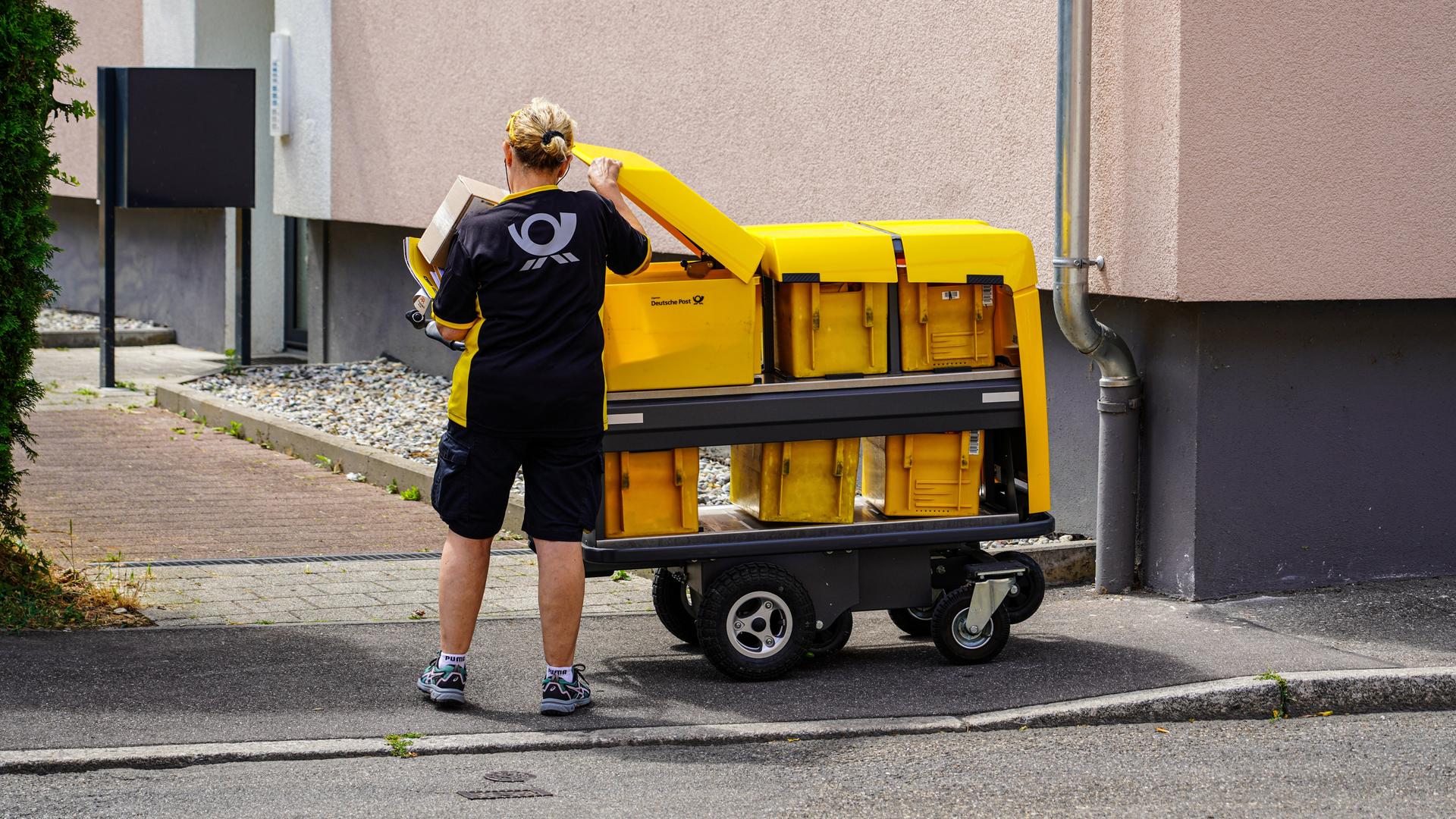 Eine Briefträgerin nimmt Briefe aus ihrem modernen Postwagen der Deutschen Post, um sie in die Briefkästen eines Mehrfamilienhauses einzuwerfen. Eine Briefträgerin nimmt Briefe aus ihrem modernen Postwagen der Deutschen Post, um sie in die Briefkästen eines Mehrfamilienhauses einzuwerfen.